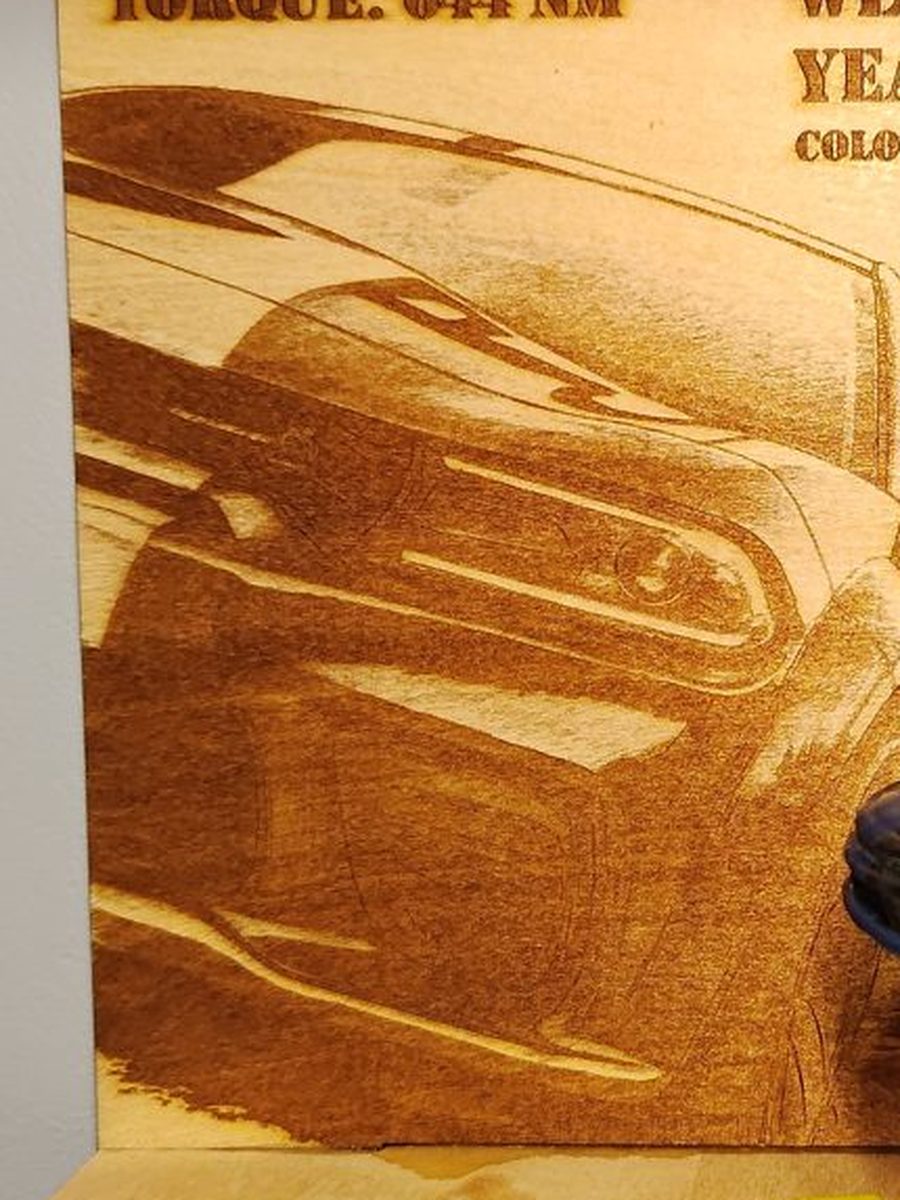 Zbliżenie na panel ze sklejki z wygrawerowanym przodem Dodge Chargera - widoczny reflektor, grill i faktura drewna